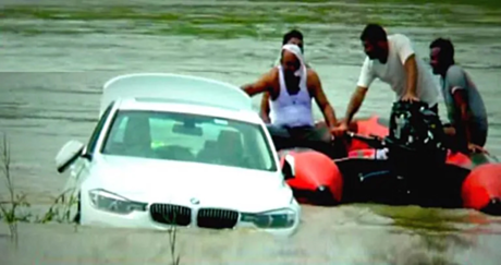 Chiếc BMW kẹt ở bãi đất giữa sông và đang được chủ nhân tìm cách đưa trở lại bờ. Ảnh: News18