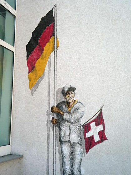 Bức ảnh người đàn ông cầm cờ của hai nước nhằm nói đến vị trí địa lý thú vị của thị trấn. Ảnh: BBC.