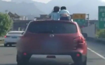Hai đứa trẻ ngồi trên nóc xe chạy cao tốc